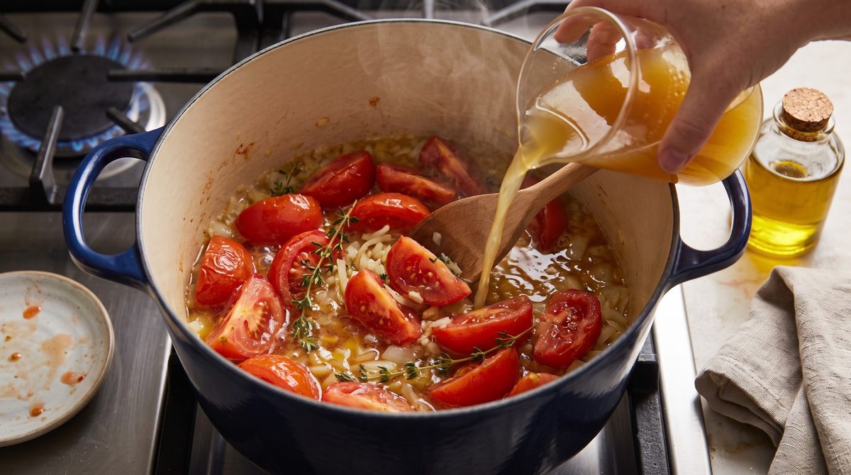 Gemüsebrühe wird aus einem Messbecher über die Tomaten im Topf gegossen